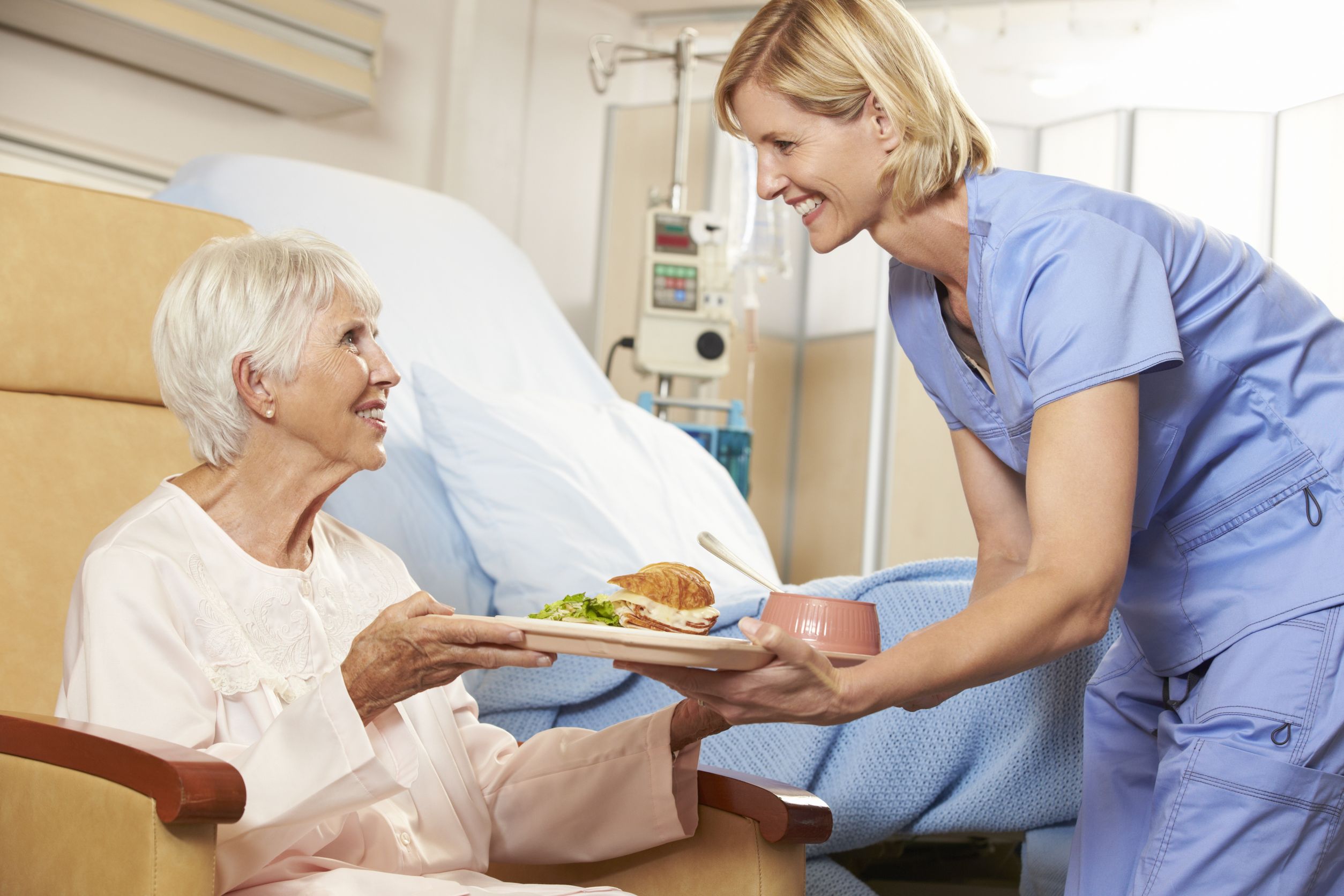 18736181_l-Nurse-Serving-Meal-To-Senior-Female-Patient-Sitting-In-Chair